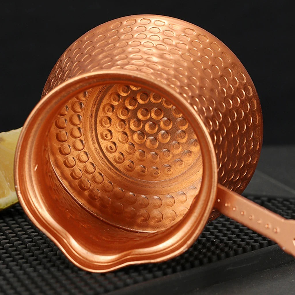 Copper Turkish coffee maker with textured design on a black background