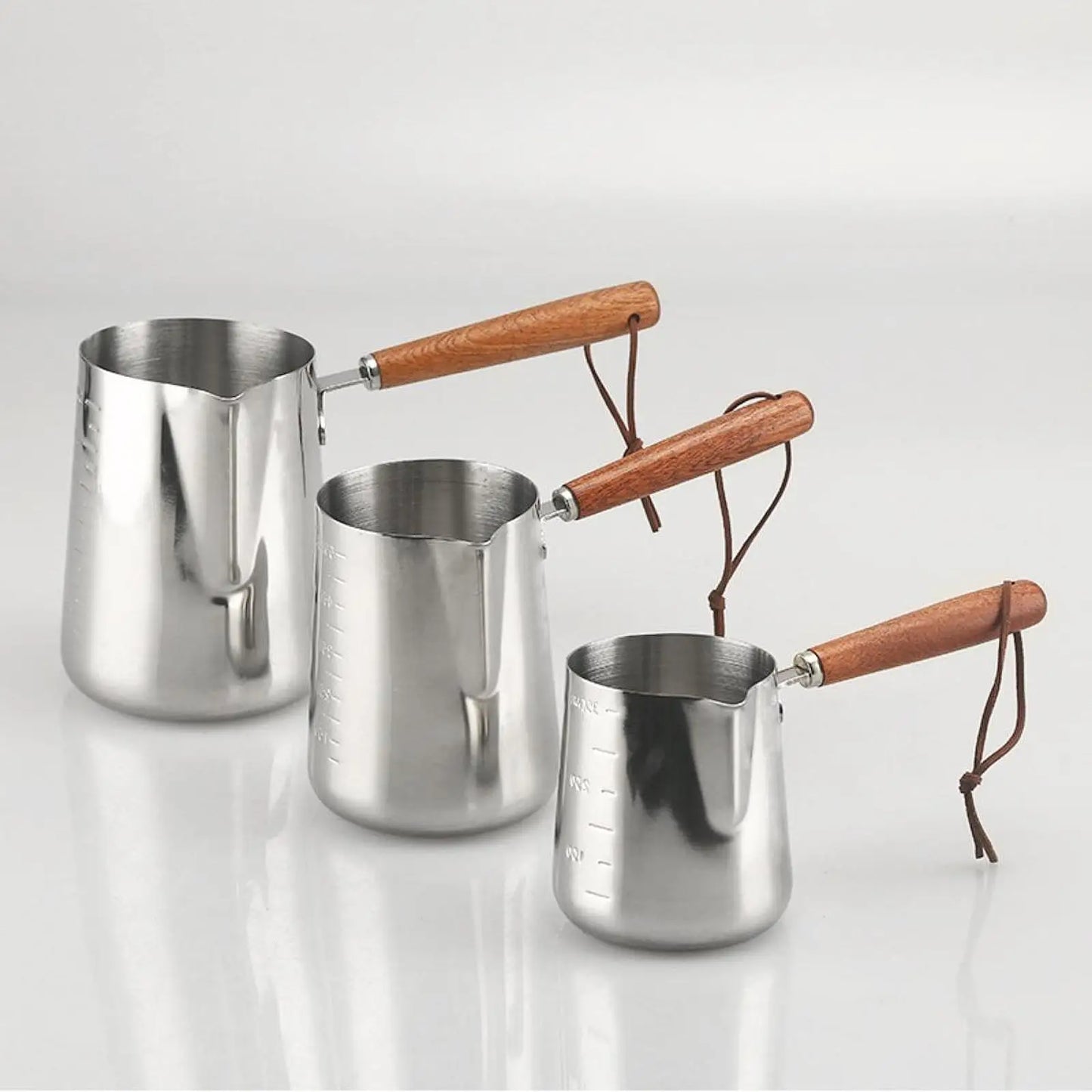 Three stainless steel Turkish coffee makers with wooden handles on a light gray background