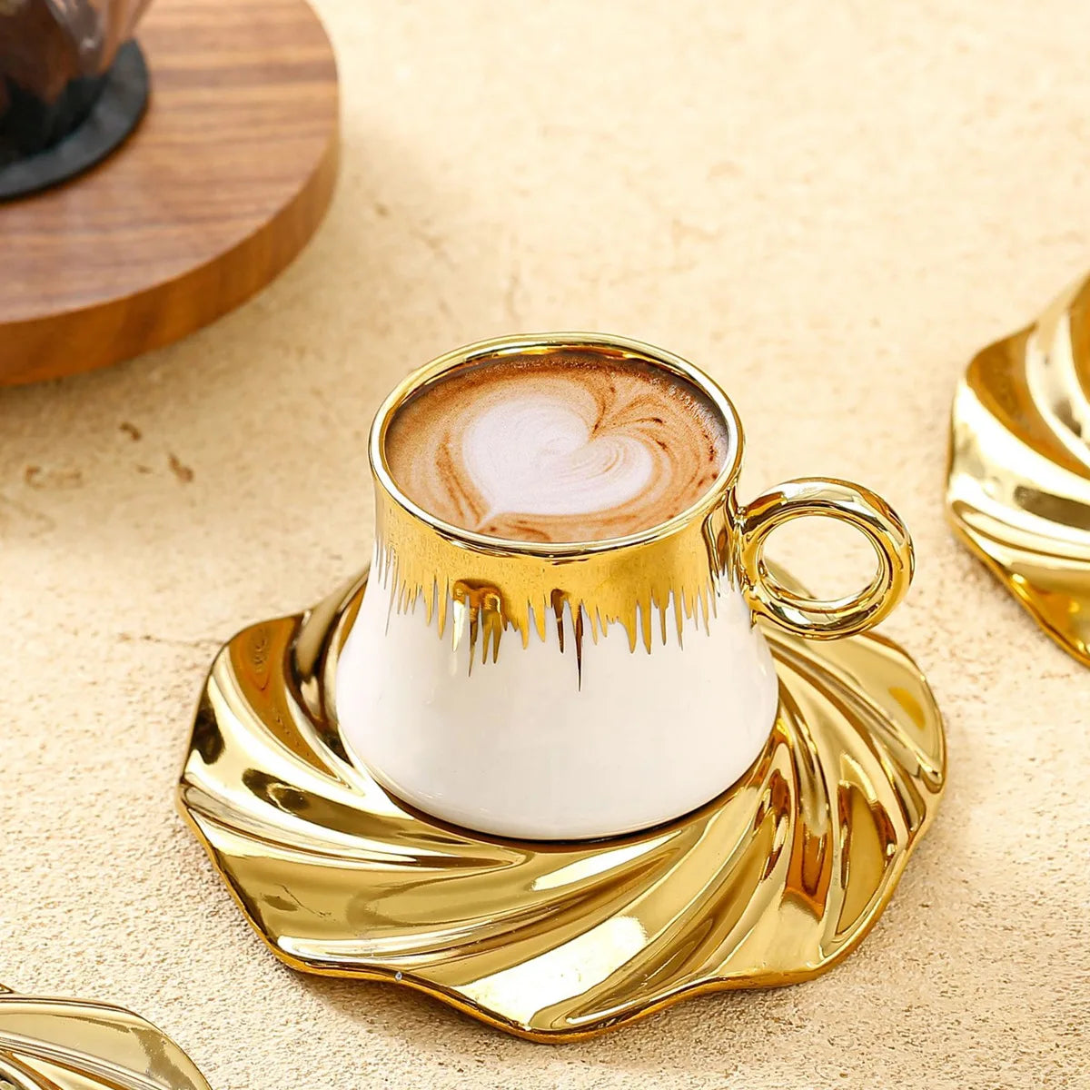 Gold-rimmed coffee cup with latte art on a matching saucer on a beige surface.