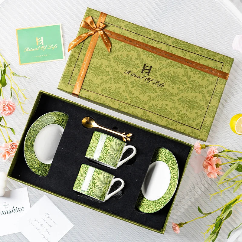 Green ceramic coffee set with matching box on a white surface with flowers.
