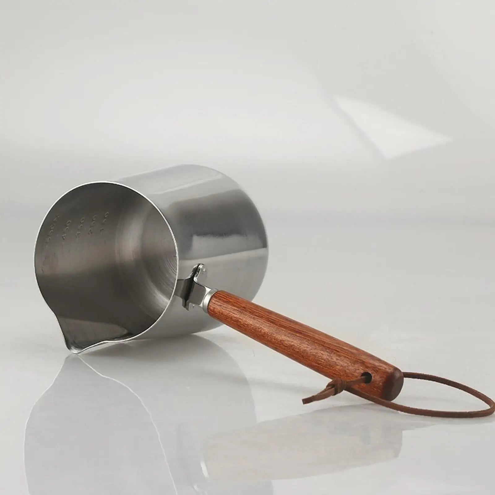 Metallic Turkish coffee maker with wooden handle on a reflective surface
