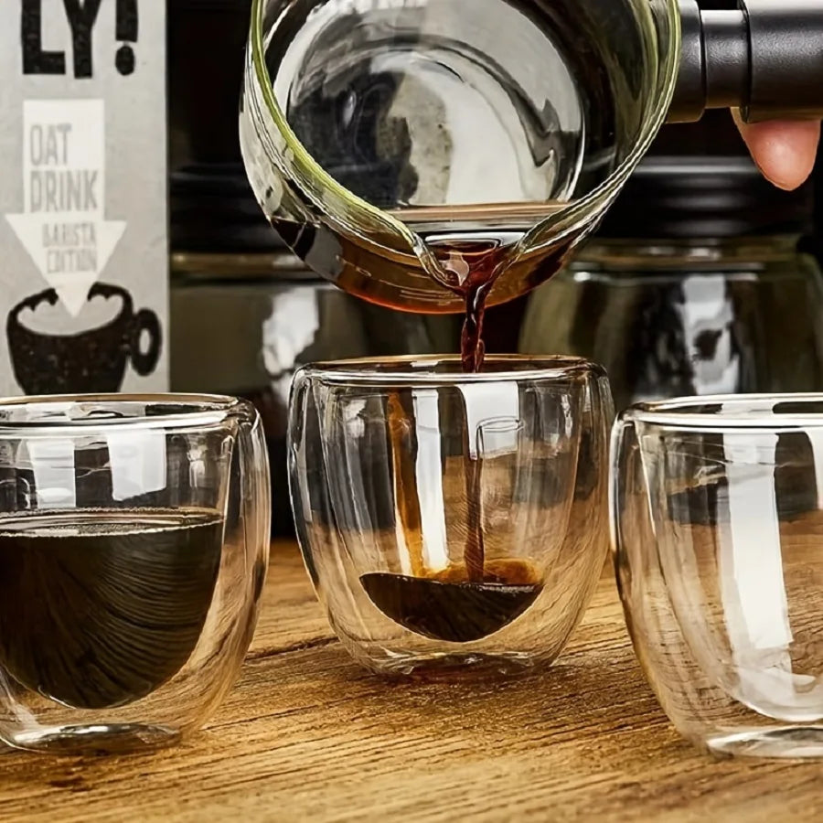Oat drink being poured from a bottle into two glass cups on a wooden surface.