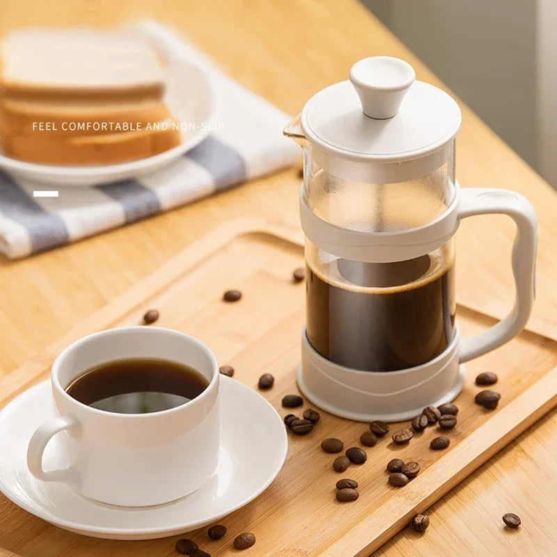 White French press filled with coffee and a cup of coffee on a wooden table with scattered coffee beans.