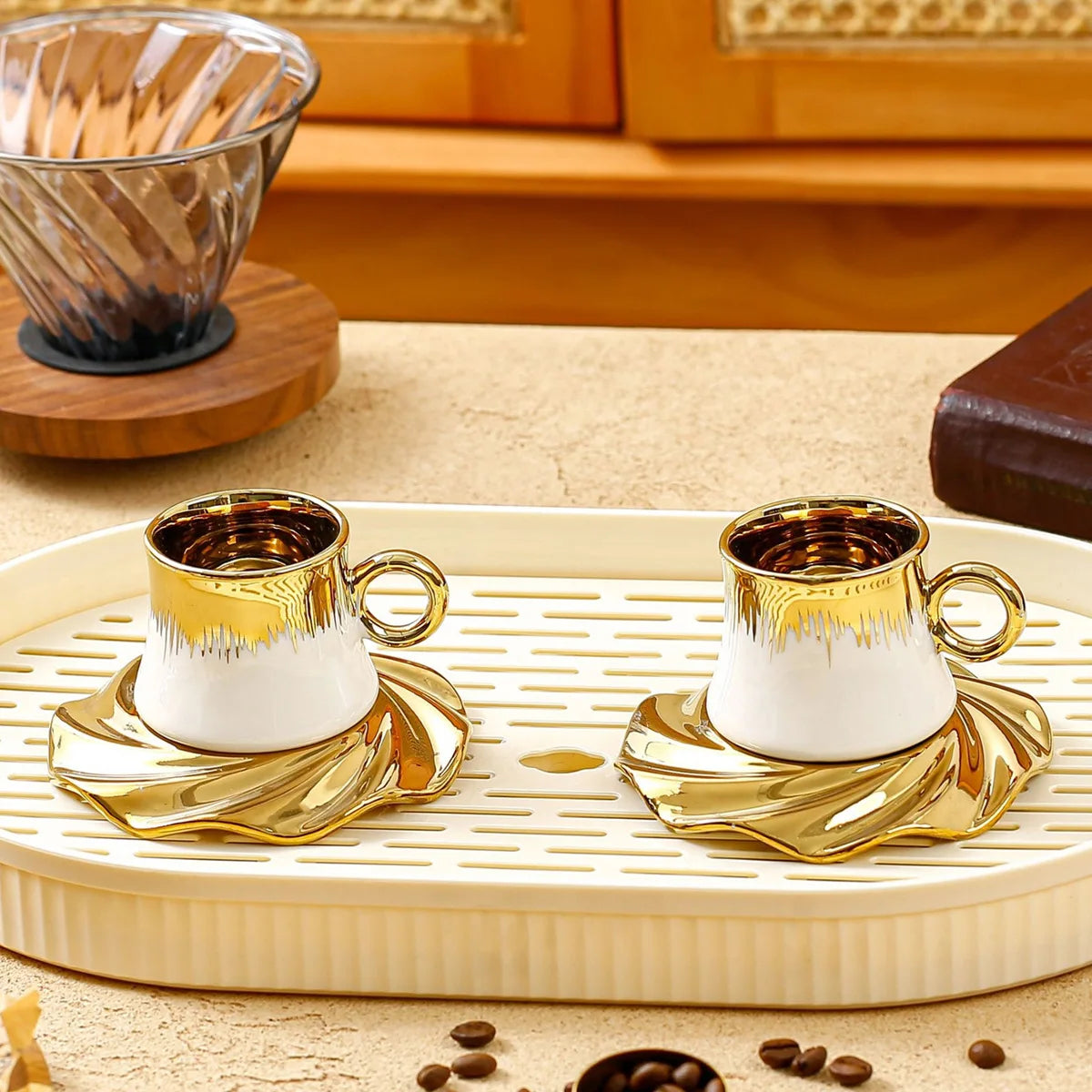 Two gold and white coffee cups on a decorative tray with coffee beans on a wooden surface.