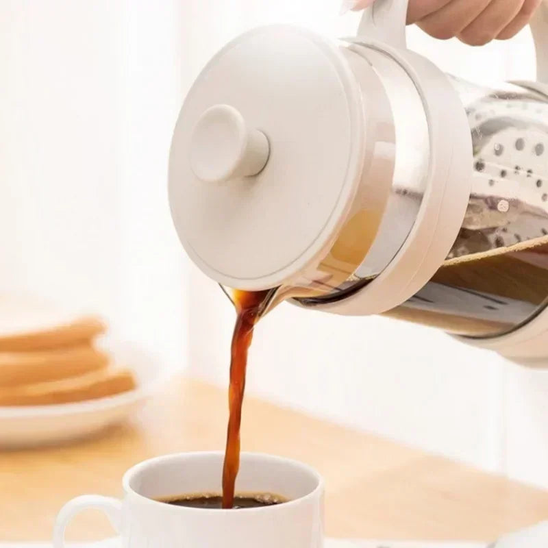 White coffee maker pouring coffee into a white cup on a light wooden surface.