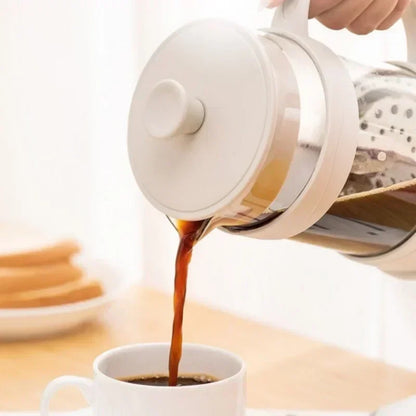 White coffee maker pouring coffee into a white cup on a light wooden surface.